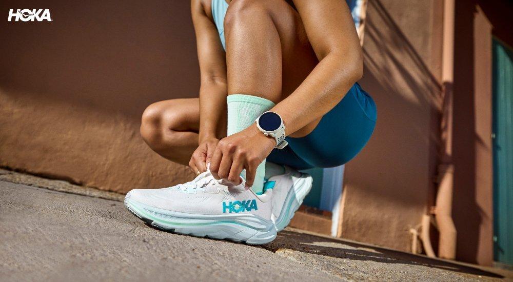 A runner lacing up some Hoka Clifton running shoes